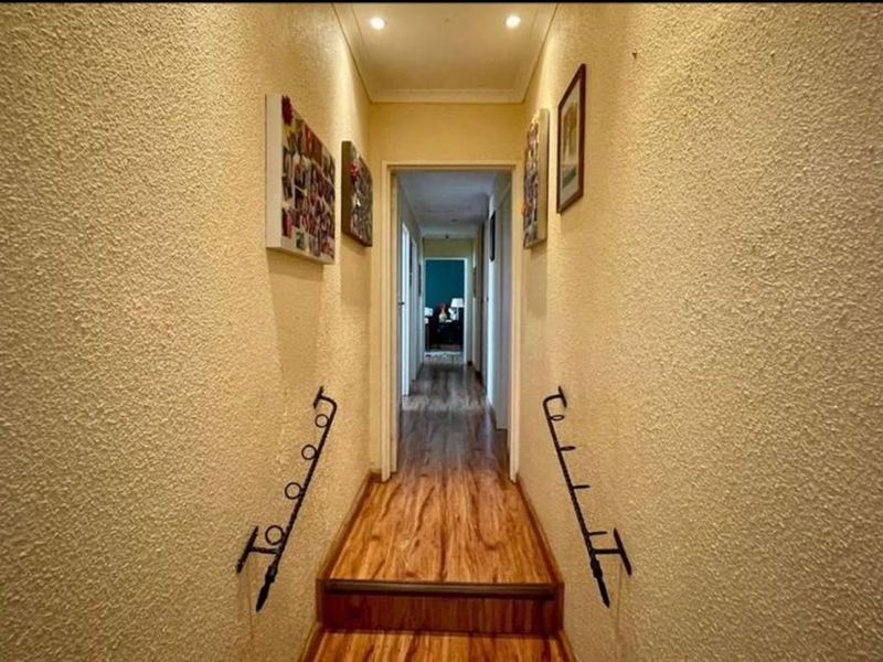 A functional hallway featuring textured walls, laminate flooring, and decorative wrought iron handrails leading to a raised transition area.