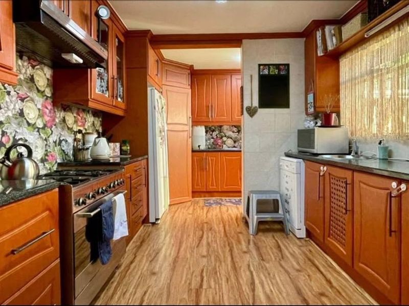A functional kitchen featuring warm-toned wooden cabinetry, granite countertops, a gas stove with extractor fan, and durable laminate flooring.