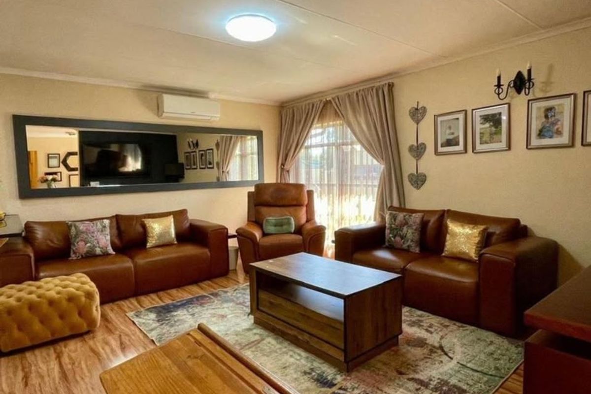 A comfortable living room featuring laminate flooring, a wall-mounted air conditioning unit, and a large decorative mirror.
