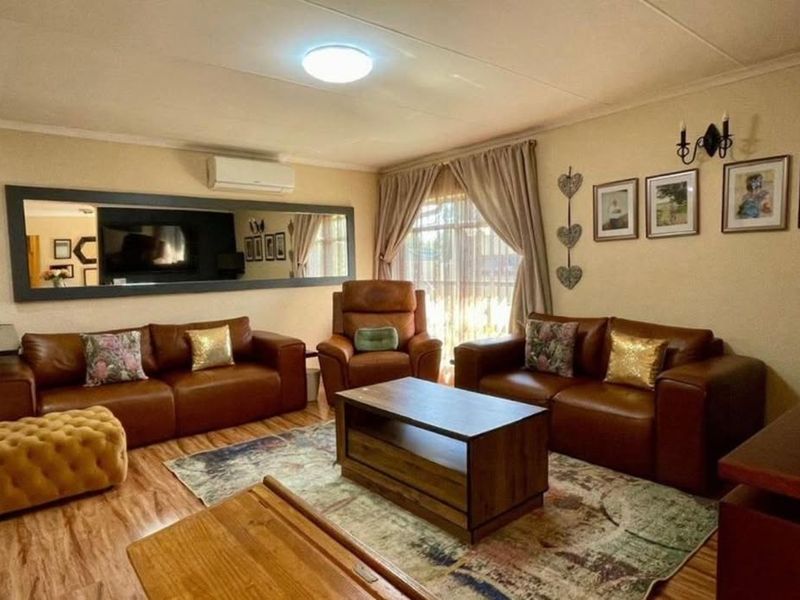 A comfortable living room featuring laminate flooring, a wall-mounted air conditioning unit, and a large decorative mirror.
