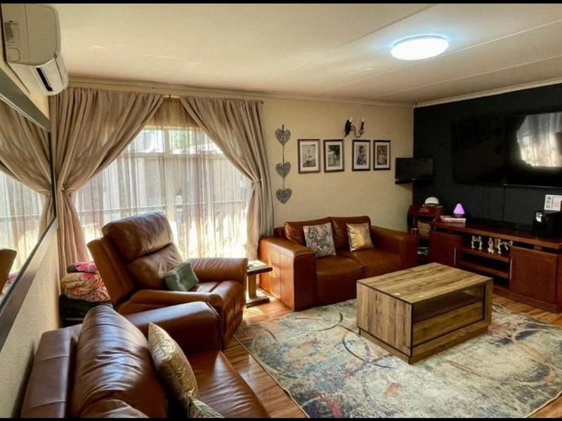 A comfortable living room featuring laminate flooring, a wall-mounted air conditioning unit, and a large window with curtains.