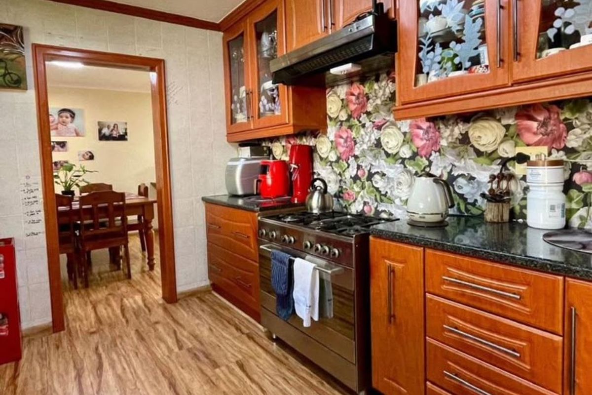 A functional kitchen featuring warm-toned wooden cabinetry, granite countertops, and a gas stove with an integrated extractor fan, leading into an adjacent dining area.