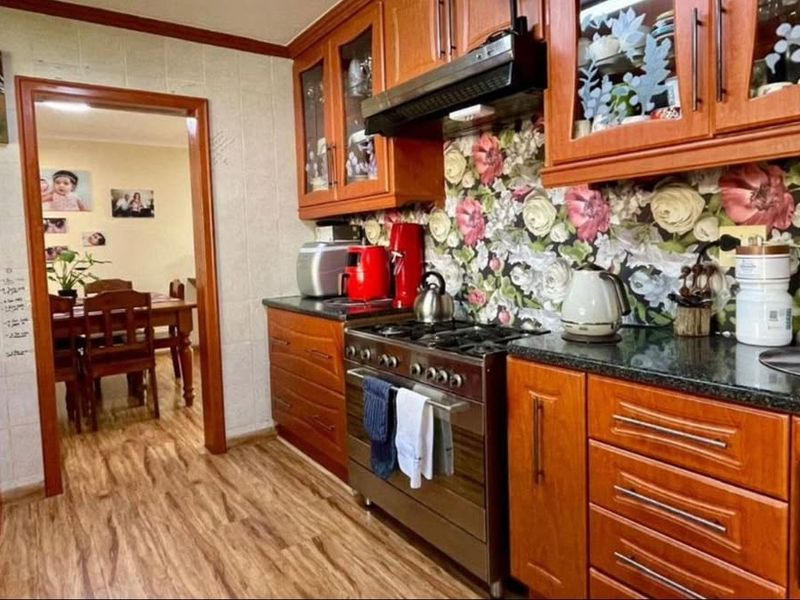 A functional kitchen featuring warm-toned wooden cabinetry, granite countertops, and a gas stove with an integrated extractor fan, leading into an adjacent dining area.