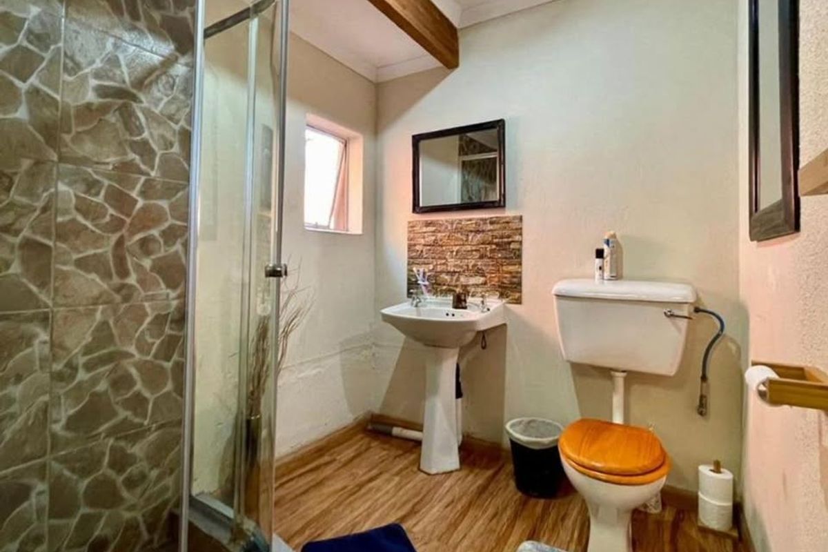 Compact bathroom featuring a pedestal basin, toilet, and shower enclosure with decorative tiled accents and laminate flooring.