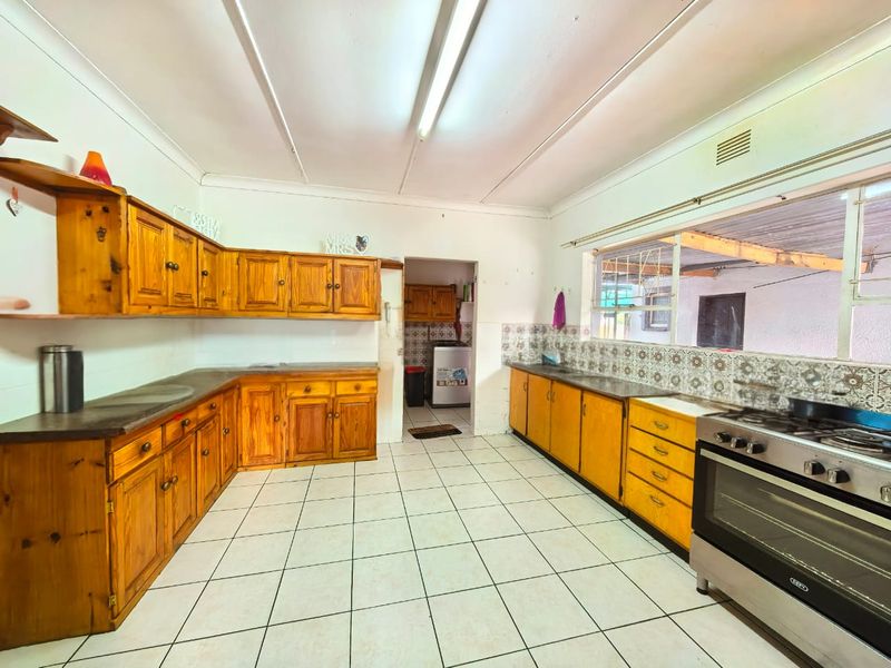 Spacious kitchen featuring traditional wooden cabinetry, tiled flooring, a tiled backsplash, and a freestanding oven, offering a functional layout with potential for modernization.