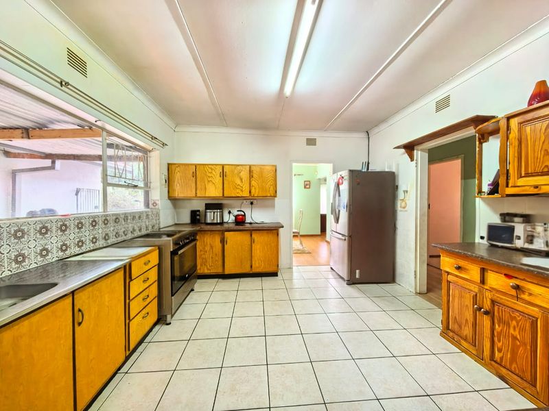 A functional kitchen featuring wooden cabinetry, tiled flooring, and a patterned backsplash, offering a dated aesthetic with potential for modern renovation.