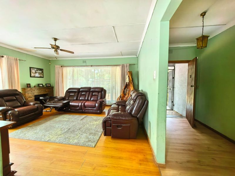 Spacious living room featuring laminate flooring, a stone-clad fireplace, and a ceiling fan, with direct access to an adjacent hallway.
