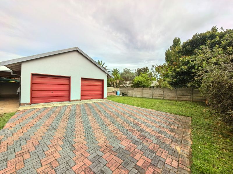 Exterior view of a double garage with red doors, featuring a paved driveway and a private garden area with boundary walling.