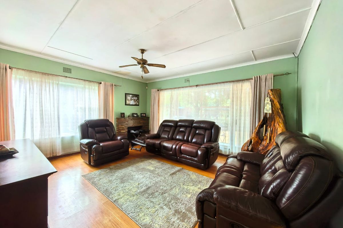 Spacious living room featuring hardwood flooring, a ceiling fan, and a fireplace, with large windows providing ample natural light.