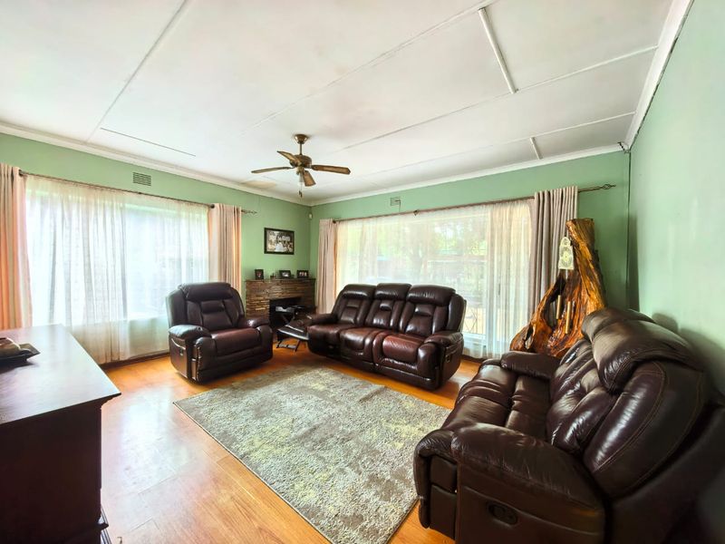 Spacious living room featuring hardwood flooring, a ceiling fan, and a fireplace, with large windows providing ample natural light.