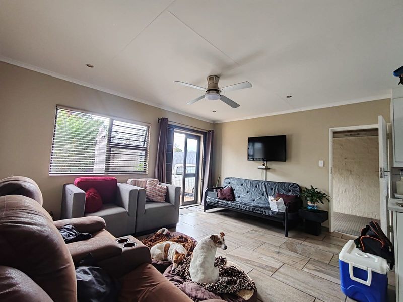 A living room featuring tiled flooring, a ceiling fan, and direct access to the exterior through an aluminium door.