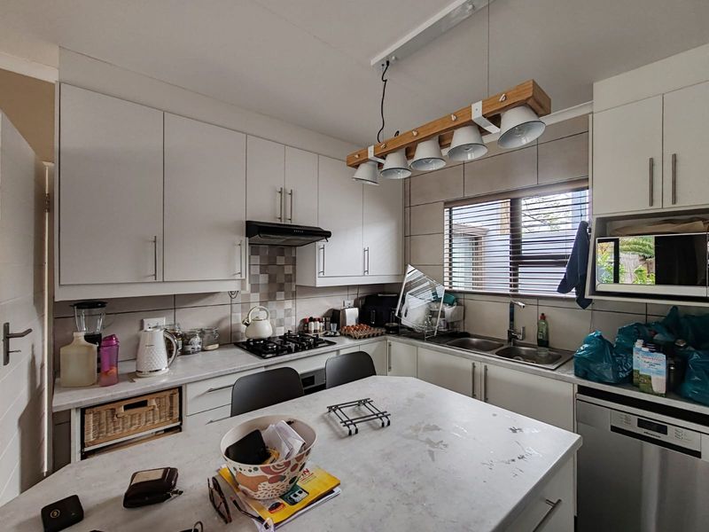 A functional kitchen featuring white cabinetry, a gas hob, extractor fan, double sink, and a central island with a laminate countertop.