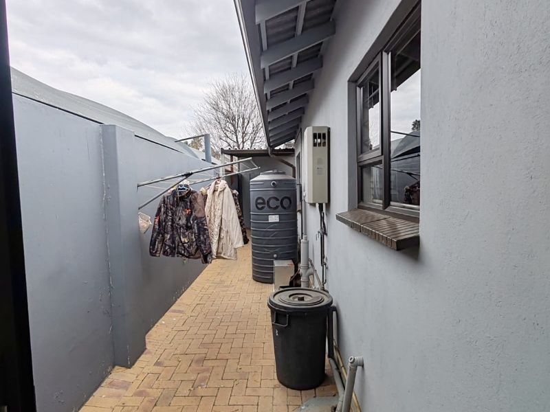 A functional side utility area featuring brick paving, a water storage tank, and a wall-mounted gas geyser unit.