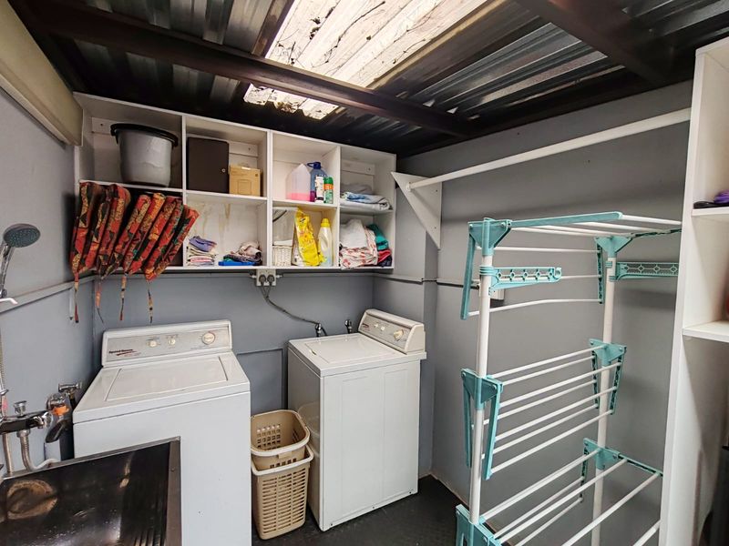 Functional laundry area featuring built-in shelving, utility sink, and plumbing connections under a corrugated metal roof with a translucent panel for natural light.