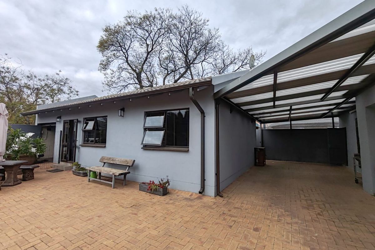 Rear exterior view of the cottage featuring a paved patio area, a covered carport, and well-maintained exterior walls with modern aluminium window frames.