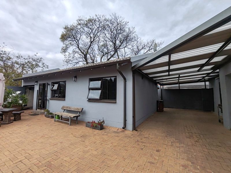 Rear exterior view of the cottage featuring a paved patio area, a covered carport, and well-maintained exterior walls with modern aluminium window frames.