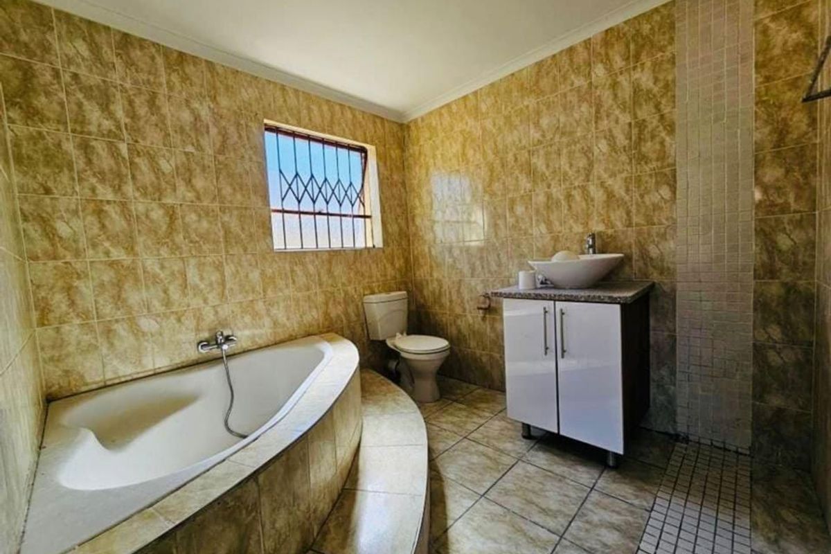 A functional bathroom featuring a corner bathtub, vanity with vessel sink, toilet, and full-height wall tiling.