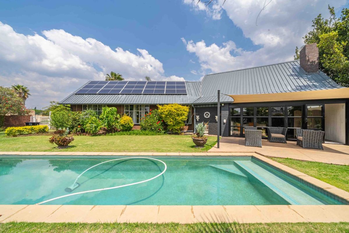 Rear view of the house featuring a swimming pool, covered patio area, metal roofing, and installed solar panels set within a landscaped garden.