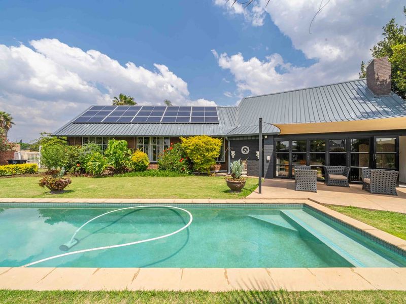 Rear view of the house featuring a swimming pool, covered patio area, metal roofing, and installed solar panels set within a landscaped garden.