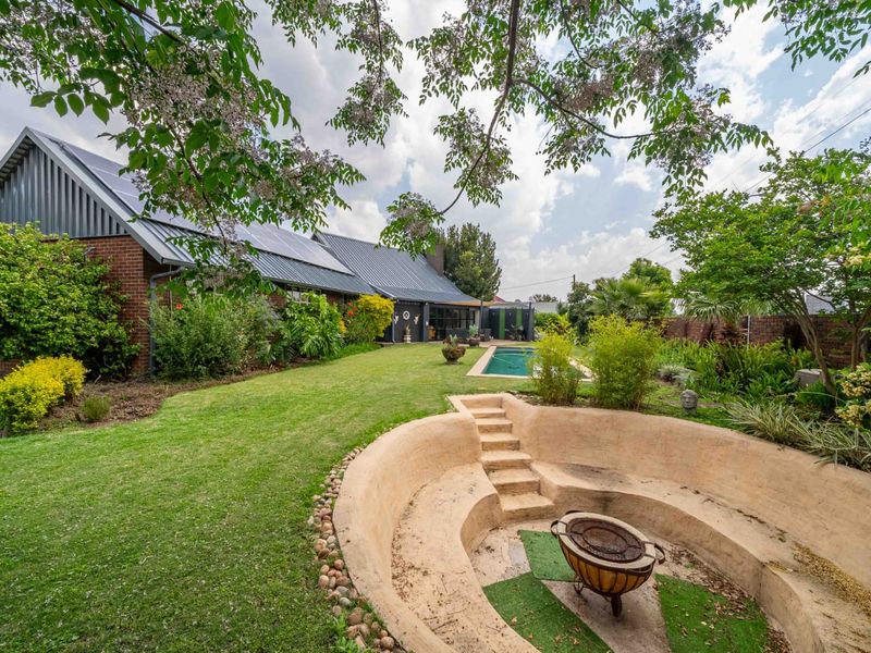 Spacious rear garden featuring a swimming pool, a unique sunken fire pit area, and a brick home with solar panels installed on the roof.