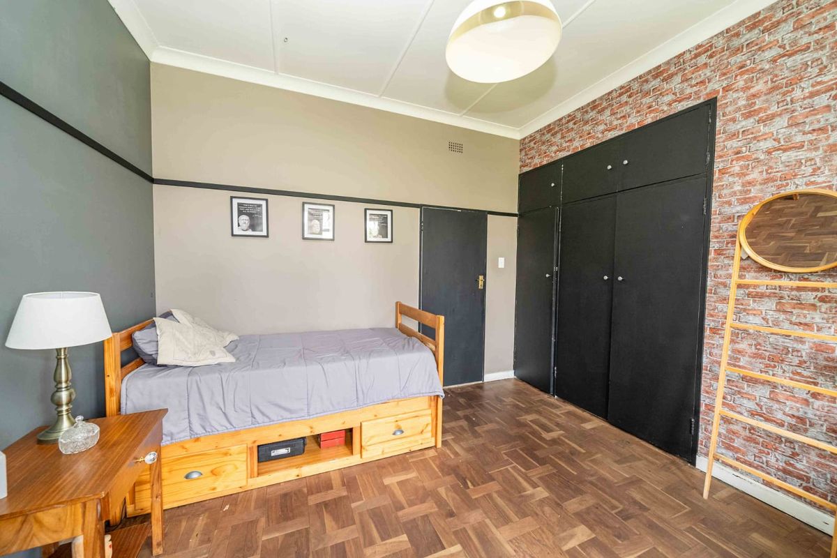 A bedroom featuring parquet flooring, built-in cupboards, and a decorative brick-effect feature wall.
