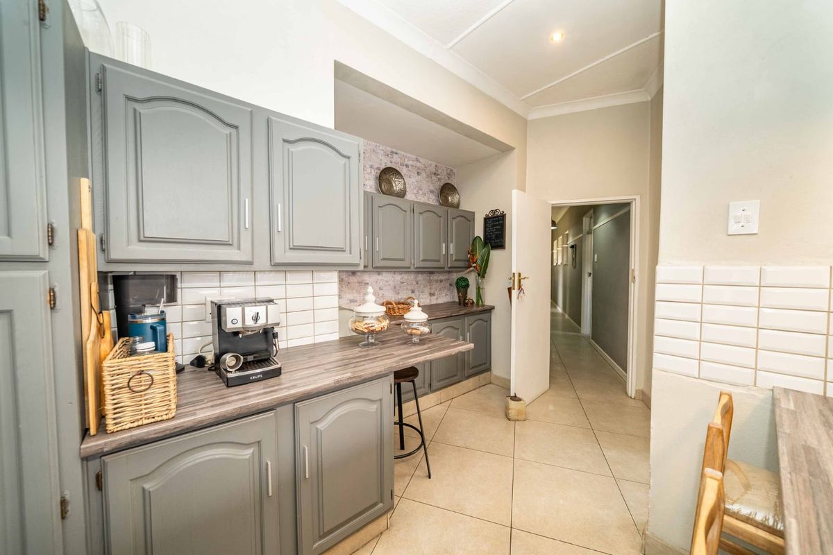A functional kitchen featuring grey cabinetry, laminate countertops, and a subway tile backsplash, leading into a hallway with tiled flooring throughout.
