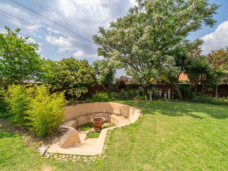 A well-maintained garden featuring a unique sunken fire pit area, mature trees, and established landscaping enclosed by a brick boundary wall.