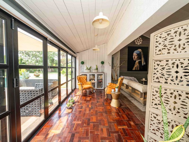 A bright, enclosed patio featuring timber parquet flooring, a white tongue and groove ceiling, and large black-framed glass stacker doors opening to the pool area.