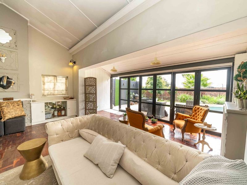 Spacious living room featuring vaulted ceilings, rich parquet flooring, and large black-framed folding glass doors that provide seamless access to the outdoor area.
