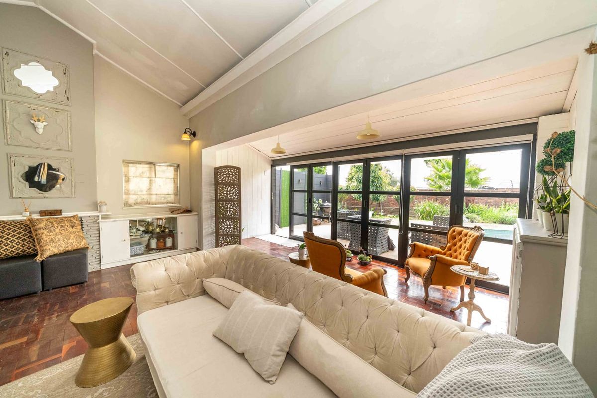 Spacious living room featuring vaulted ceilings, rich parquet flooring, and large black-framed folding glass doors that provide seamless access to the outdoor area.