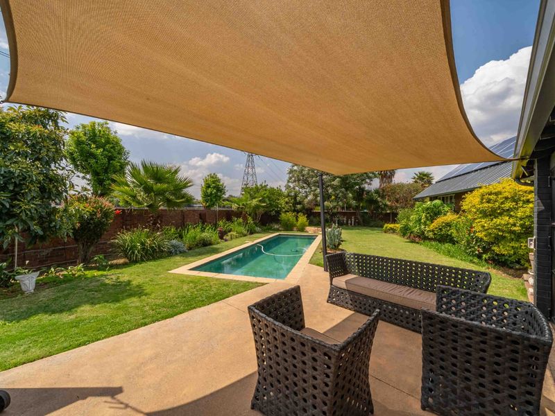 Outdoor entertainment area featuring a swimming pool, concrete patio, and a large shade sail, set within a well-maintained garden with brick boundary walls.