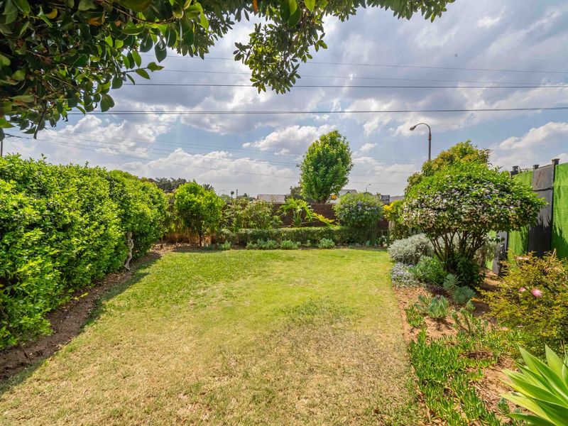 A well-maintained private garden featuring a central lawn area, established hedging, and landscaped garden beds.