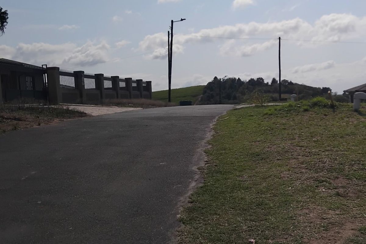 A view of the paved street and surrounding landscape, showing utility infrastructure and perimeter fencing along the residential property boundary.