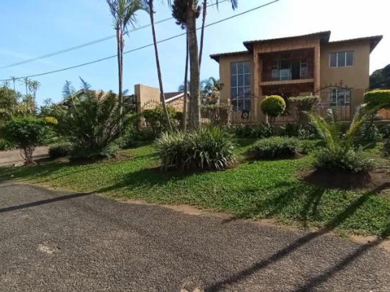 A view of the front elevation of a two-story house featuring a landscaped garden, paved driveway, and a balcony.