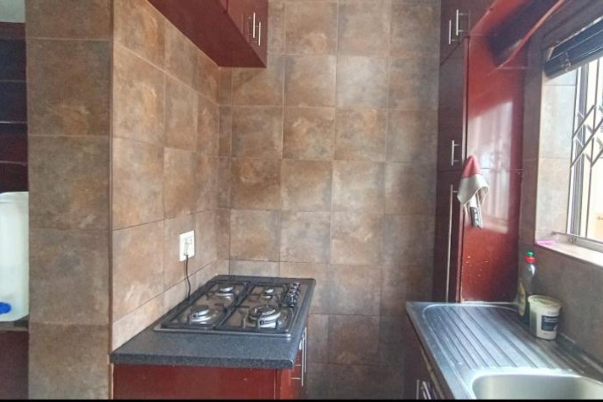 A compact kitchen featuring dark wood cabinetry, a gas hob, and a stainless steel sink with tiled splashbacks.
