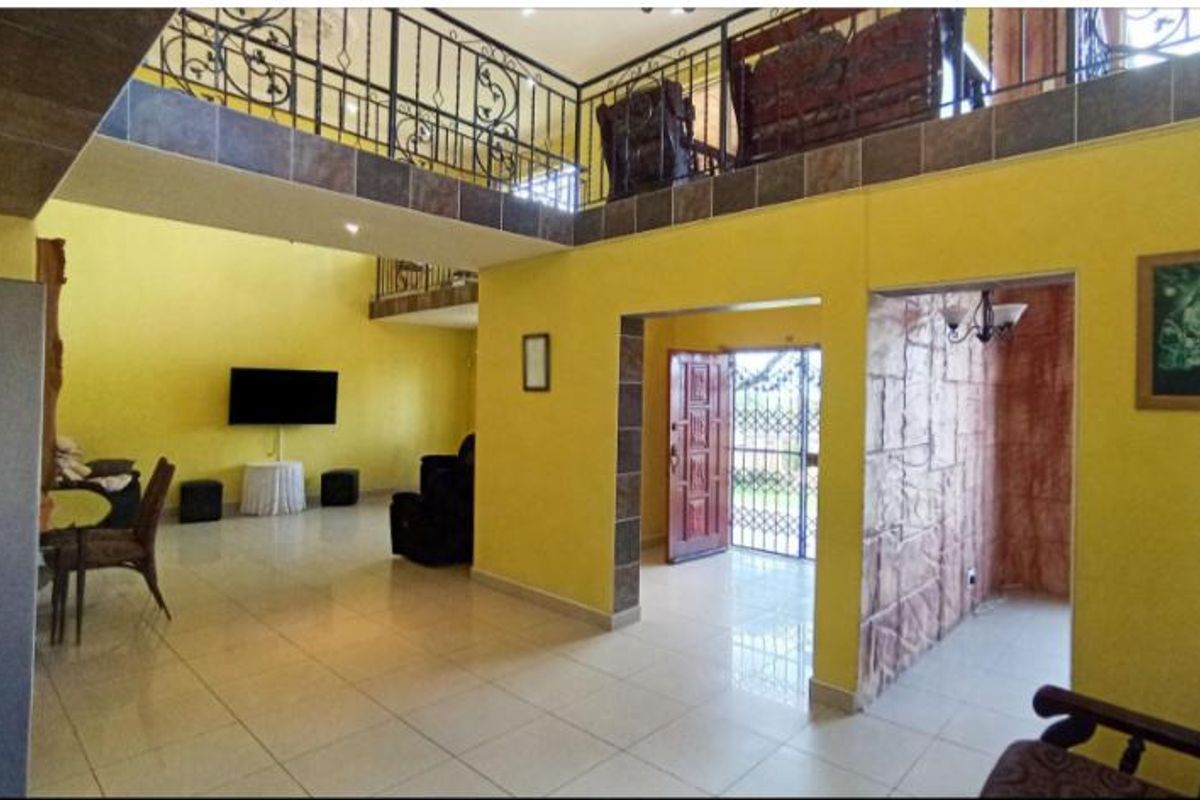 Spacious open-plan living area featuring a mezzanine level with wrought iron balustrades, tiled flooring, and a distinctive stone-clad feature wall.