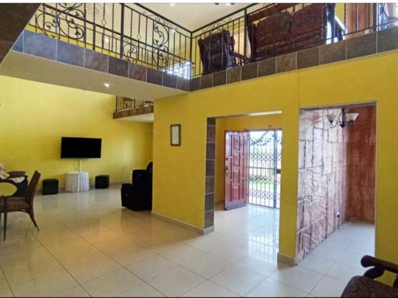 Spacious open-plan living area featuring a mezzanine level with wrought iron balustrades, tiled flooring, and a distinctive stone-clad feature wall.
