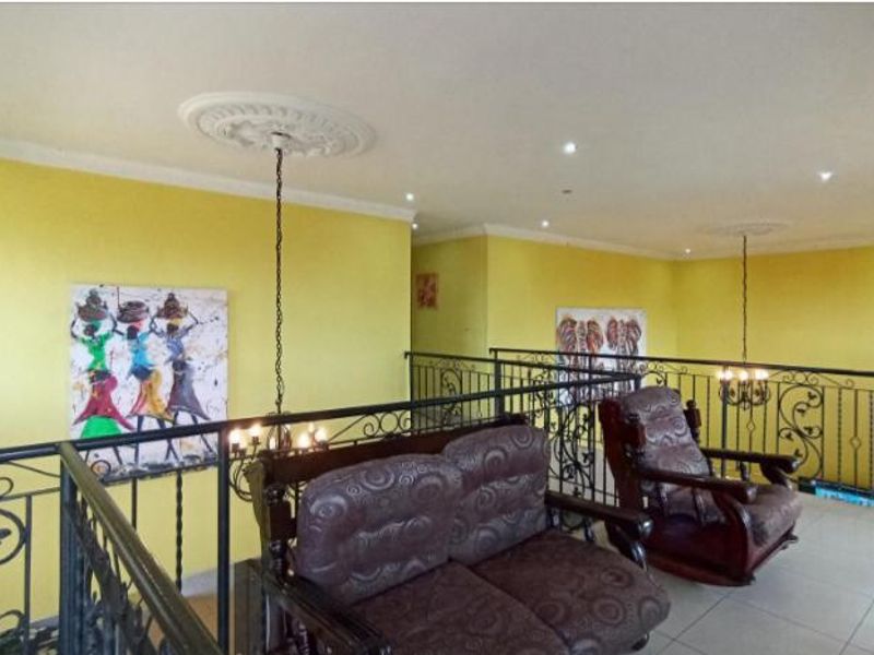 Spacious upper-level landing area featuring decorative ceiling roses, recessed lighting, and a wrought iron balustrade overlooking the lower level.