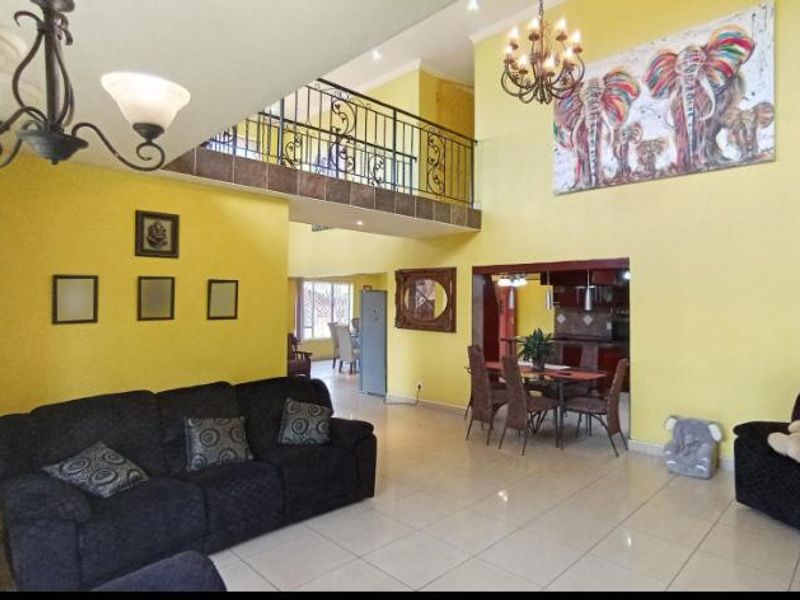 Spacious open-plan living and dining area featuring high ceilings, a mezzanine level with wrought iron railing, and tiled flooring throughout.
