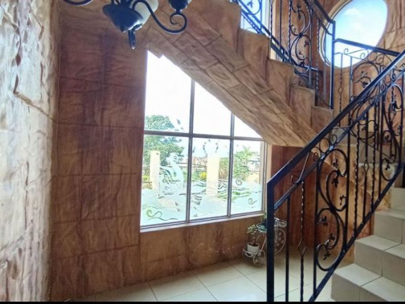 Spacious entrance hallway featuring a decorative wrought iron staircase, textured stone-effect wall finishes, and large windows providing natural light.