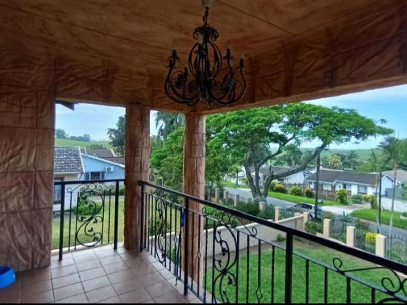 A covered balcony featuring textured stone-effect pillars, tiled flooring, and a wrought iron railing, offering an elevated view of the surrounding neighborhood.
