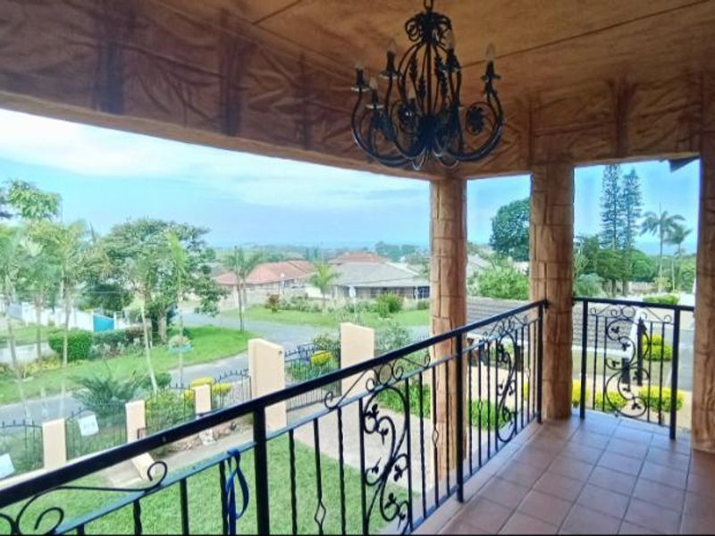 Covered balcony featuring a wrought iron balustrade, tiled flooring, and decorative stone-effect pillars, offering an elevated view of the surrounding neighborhood.