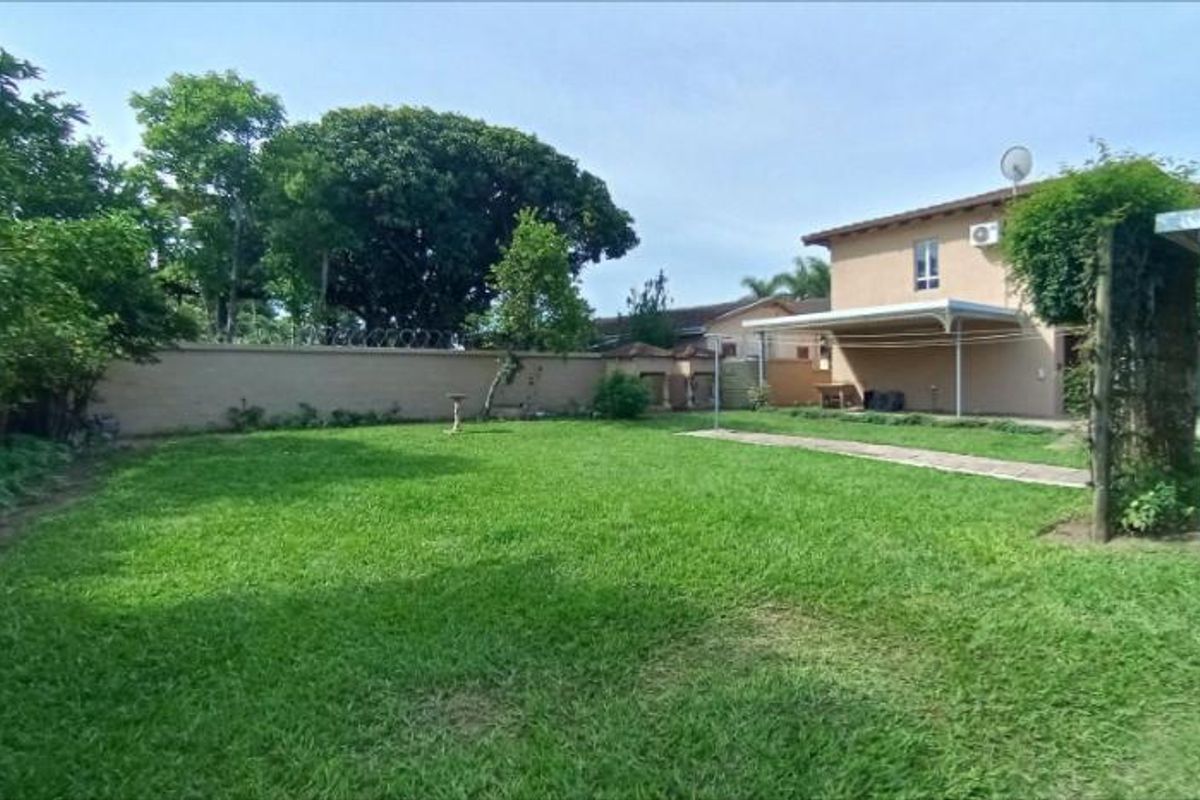 Spacious rear garden featuring a well-maintained lawn, perimeter wall, and a covered patio area attached to the main house structure.