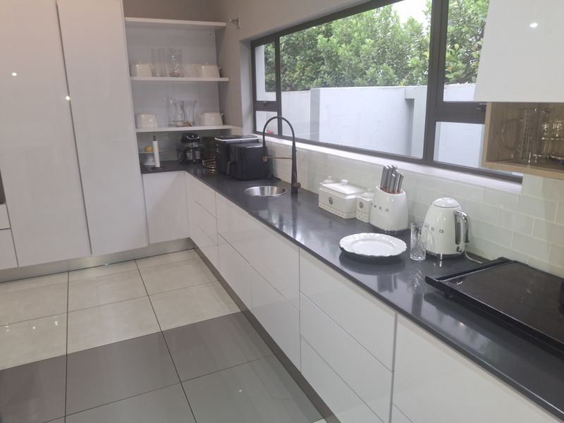 Modern kitchen featuring sleek white cabinetry, dark stone countertops, a subway tile backsplash, and large windows providing ample natural light.