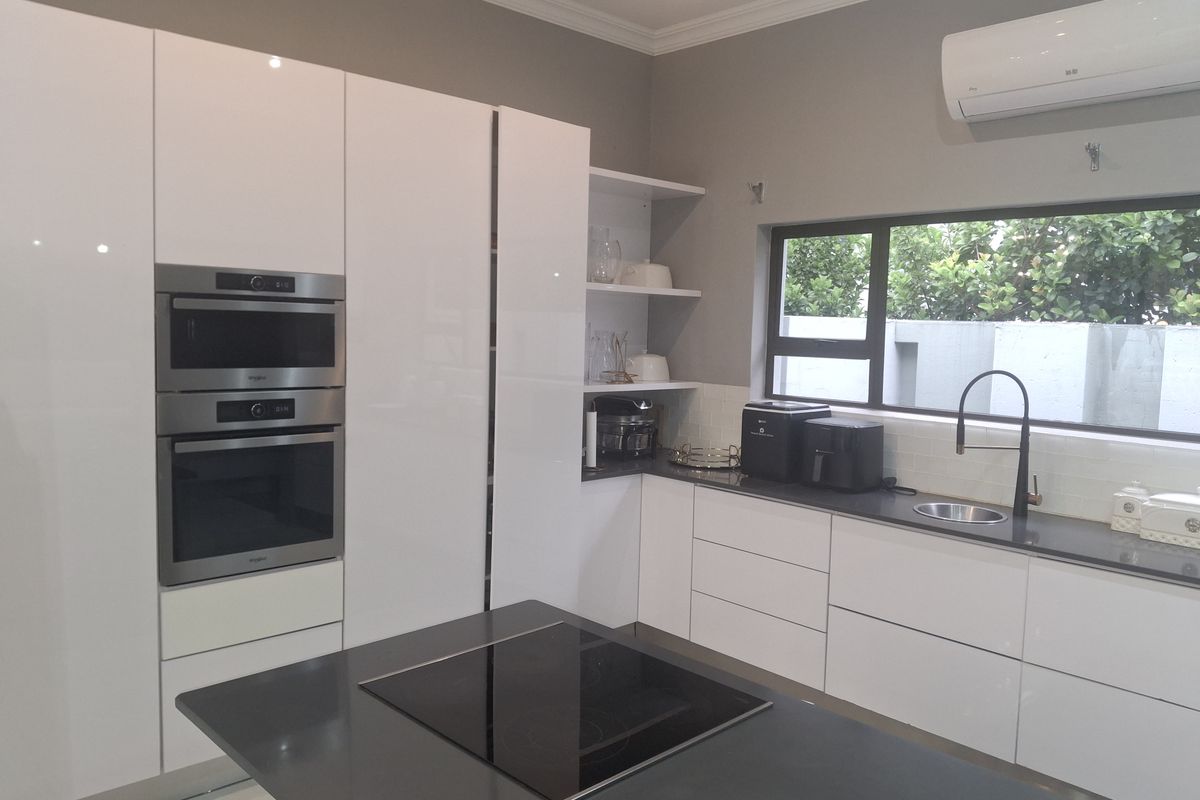 Modern kitchen featuring high-gloss white cabinetry, dark quartz countertops, a central island with an induction hob, and integrated stainless steel appliances.
