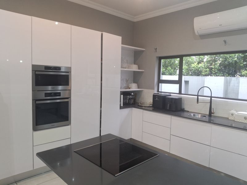 Modern kitchen featuring high-gloss white cabinetry, dark quartz countertops, a central island with an induction hob, and integrated stainless steel appliances.