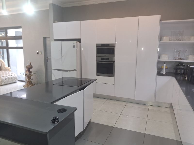 Modern kitchen featuring sleek white glossy cabinetry, dark quartz countertops, a central island with an induction cooktop, and integrated stainless steel appliances.