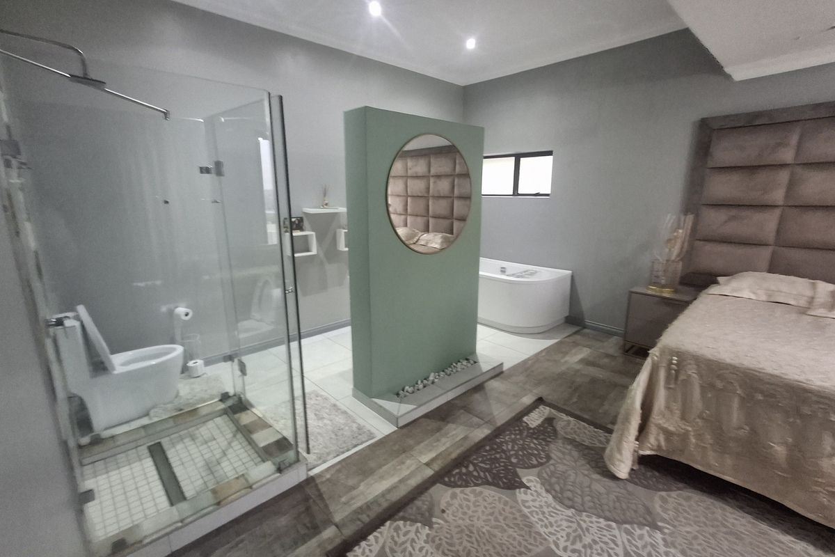 Spacious bedroom featuring an open-plan en-suite layout with a glass-enclosed shower, freestanding bathtub, and a modern central partition wall.
