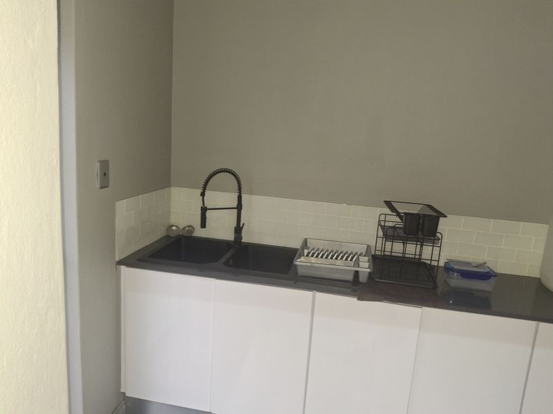 A functional scullery area featuring a modern double basin sink with a gooseneck tap, white cabinetry, and a clean subway tile backsplash.