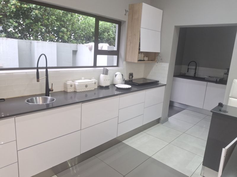 Modern kitchen featuring sleek white cabinetry, dark stone countertops, subway tile backsplash, and a secondary scullery area visible through the doorway.